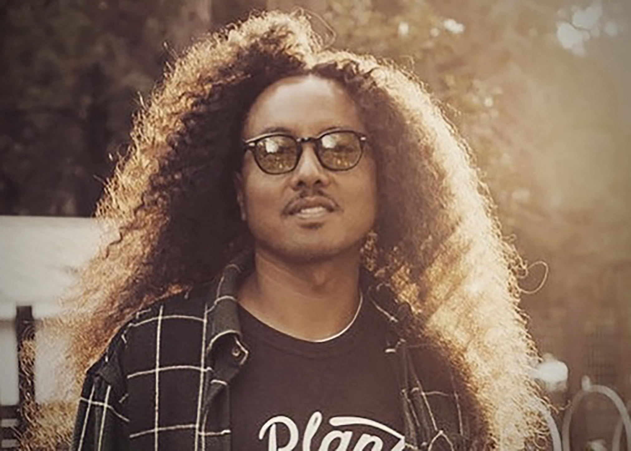 person with long brown hair, glasses. wearing a plaid button up over a black tshirt
