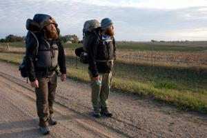 two veterans pause in the middle of road amid their backpacking trip