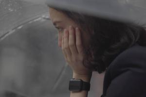 Film still of a pensive Shiori under an umbrella, face in hand