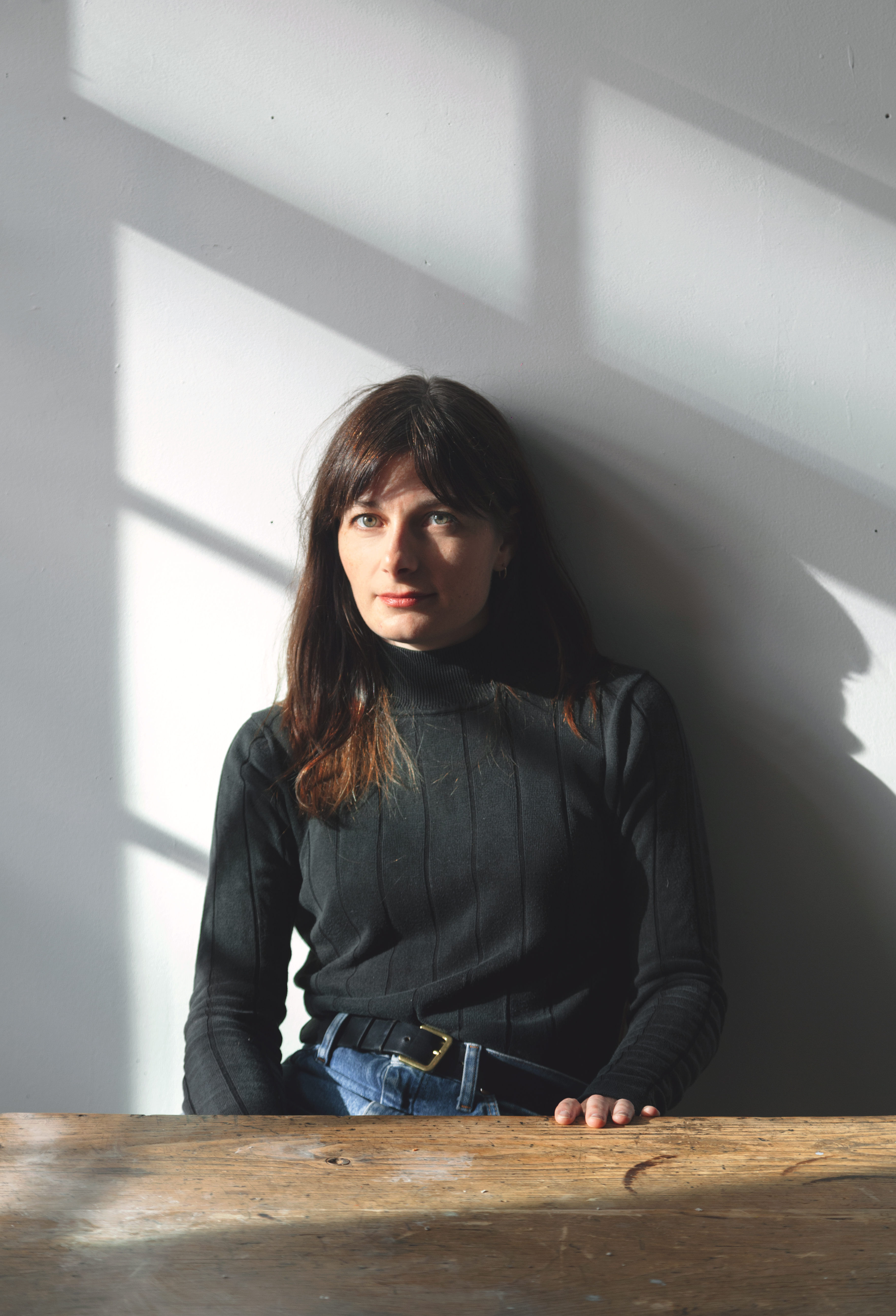woman with black long sleeve shirt and long brown hair, sitting at a brown wooden table.