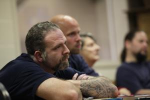 middle aged white male convict listens with arms crossed at a re-entry training