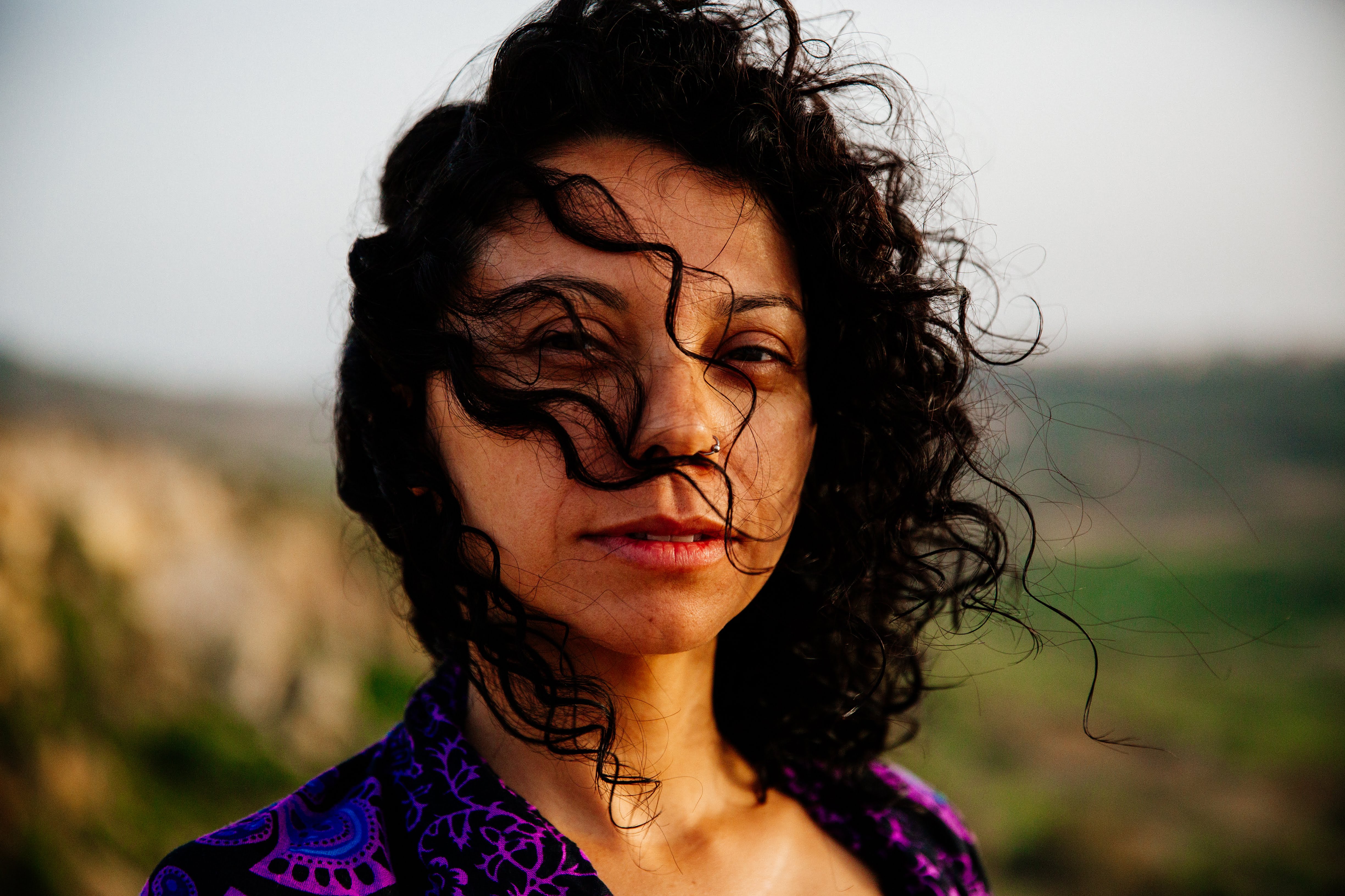 Woman with brown curly hair swept across her face, wearing a purple top.