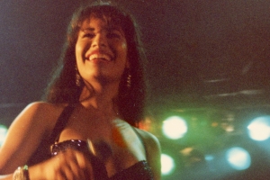 Grainy photograph of the singer Selena, standing in front of bright stage lights.