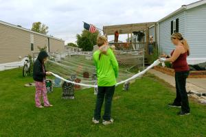 two young children hang Halloween decorations with their mother outside their mobile home