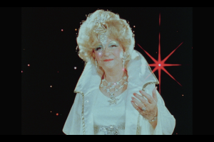 Ruth E. Norman dressed in white elaborate clothes beckons towards us with her hand out.