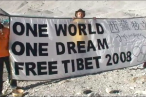 three men in orange jackets hold a banner which reads "one world, one dream, free Tibet 2008"