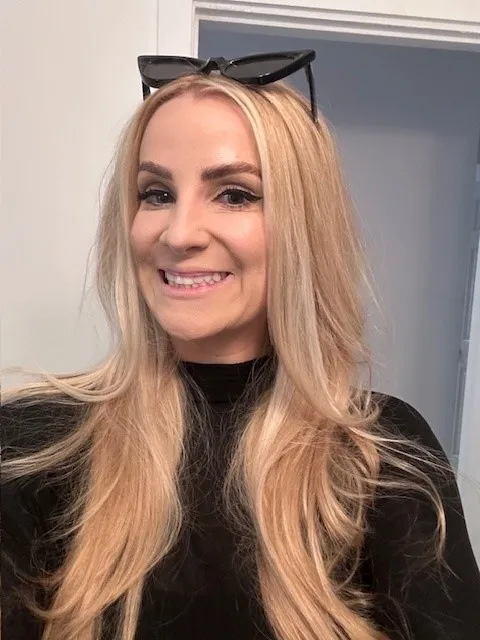 Headshot of adult with light skin tone, long blond hair, and black top.