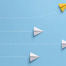 Four paper airplanes fly across a sky blue backdrop. The bottom three are white and the top one is yellow and going off course. 