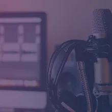 A pair of headphones hanging from a microphone with a pop filter attached to it. 