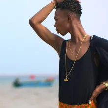 James, a young activist with Black skin wearing a black tank top, orange pants and gold jewelry, looks off behind him. A still from the film 'The Legend of the Underground.' Courtesy of HBO. 