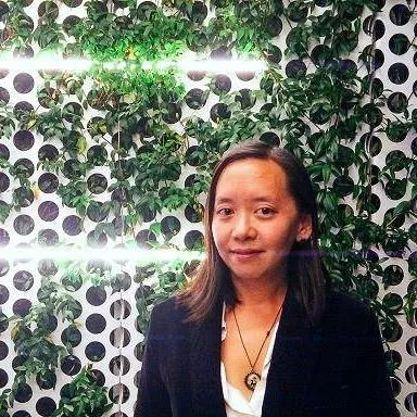 Headshot of a middle-aged Chinese American female with shoulder-length, straight black hair in a black velvet blazer and white blouse, in front of a leaves-strewn white lattice.